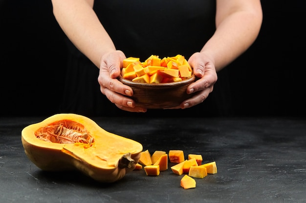 Pumpkin pieces in wooden bowl in woman hands on black