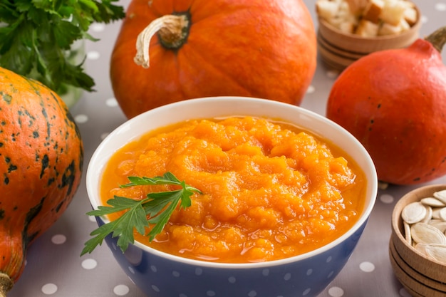 Pumpkin porridge in a bowl among orange pumpkins and seeds