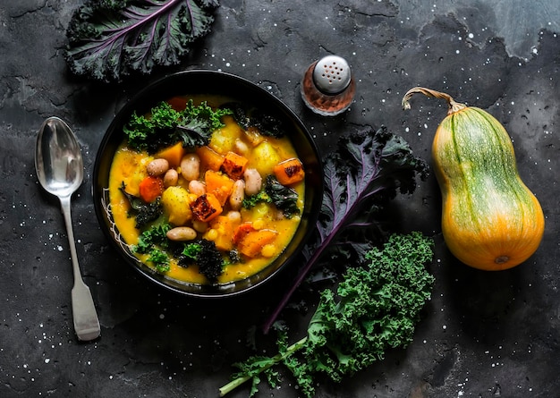 Photo pumpkin potatoes beans and kale stewed vegetarian autumn lunch on a dark background top view