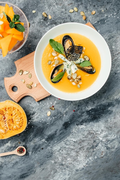 Pumpkin puree soup with pumpkin seeds, seafood, mussels, shrimps, blue cheese, mold served in bowl, vertical image. top view. place for text.