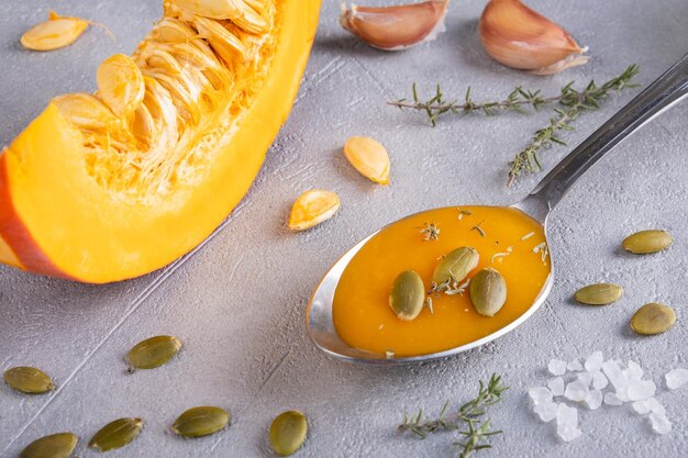 Pumpkin puree soup with pumpkin seeds and thyme in a spoon and a piece of ripe pumpkin healthy diet selective focus