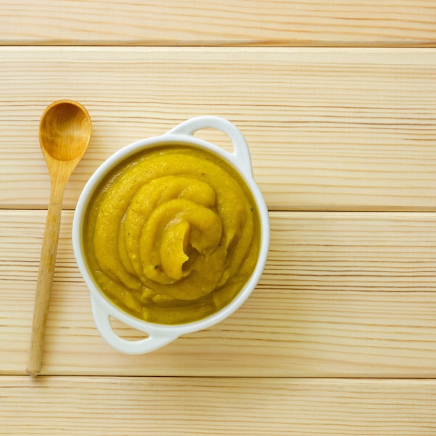 Pumpkin puree in white bowl on a light wooden background, top view.