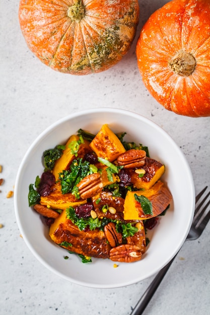 Pumpkin salad with nuts, cranberries and kale in a white bowl, top view.