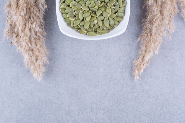 Pumpkin seeds in a bowl next to pampas grass on the marble surface