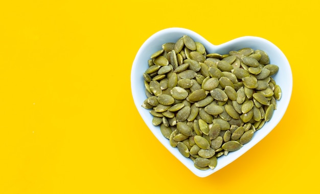 Pumpkin seeds in bowl on yellow background