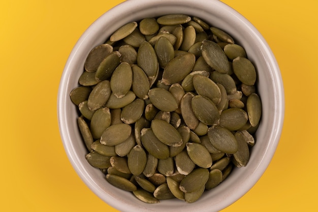 Pumpkin seeds green peeled pumpkin seeds in ceramic bowl on
yellow background copy space top view