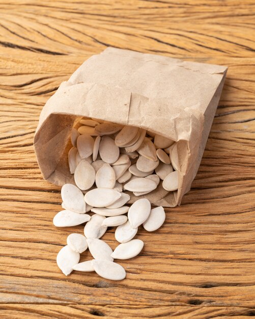 Семена тыквы в бумажном пакете над деревянным столом.