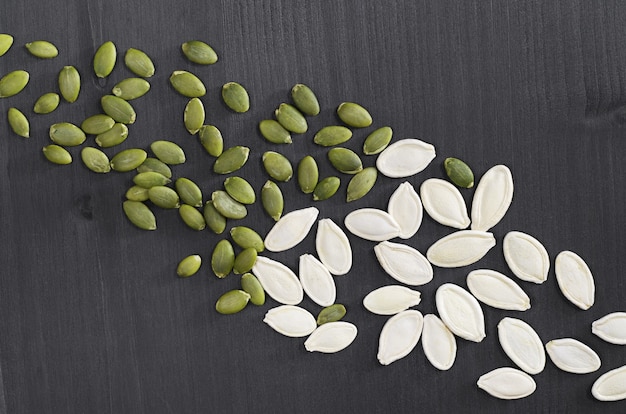 Pumpkin seeds peeled and in the shell on black wooden background, top view