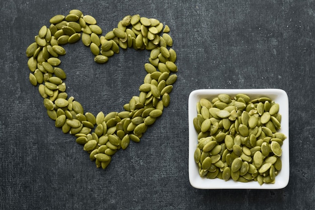 Foto semi di zucca o pepita disposti a forma di cuore, su una superficie grigia