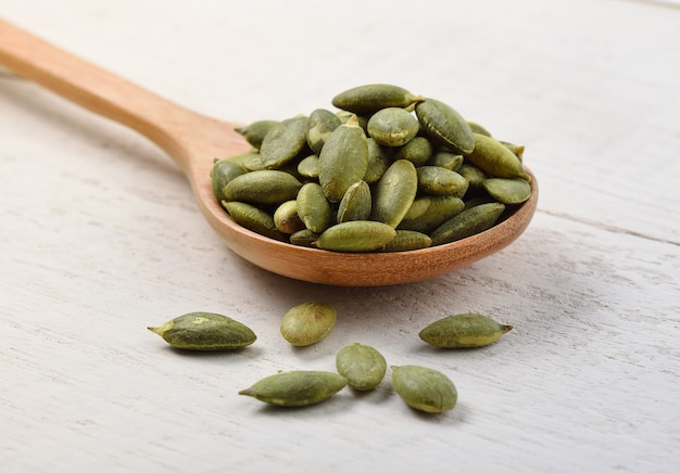 Pumpkin seeds in the spoon on white wooden