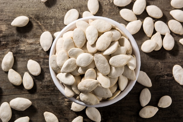 Pumpkin seeds in white bowl on wooden background Top view