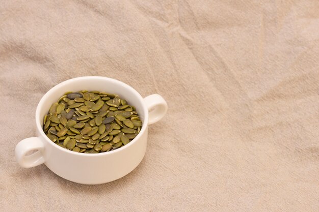 Pumpkin seeds, in a white cup on natural linen. pumpkin seeds vitamins on  brown background