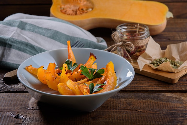 Pumpkin slices with seeds and paprika in blue plate on wooden background, autumn seasonal dish, closeup