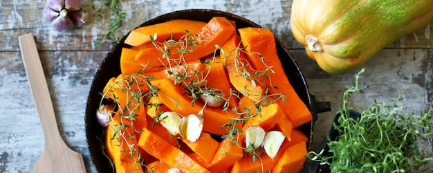 Pumpkin slices with thyme and garlic in a pan before baking. Healthy autumn food. Vegan lunch.