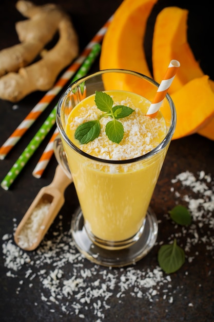 Pumpkin smoothies with ginger and coconut shavings and mint in a glass on a dark concrete surface. Healthy and delicious drink for breakfast