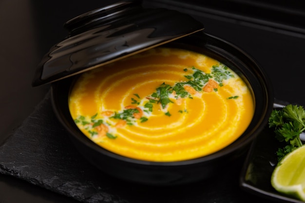 Pumpkin soup in a black plate on a black wooden background next to a slice of lemon