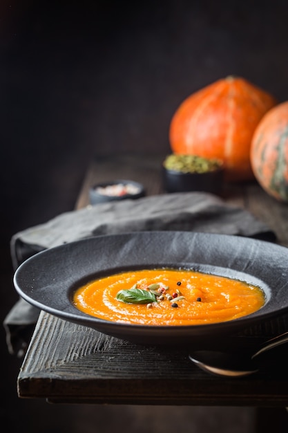 Pumpkin soup in a black plate on dark wooden. Autumn decorations.