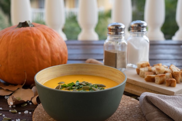 Foto zuppa di zucca in una ciotola su un tagliere di legno servita con semi di zucca e crostini di pane. zuppa vegana. fondo in legno scuro