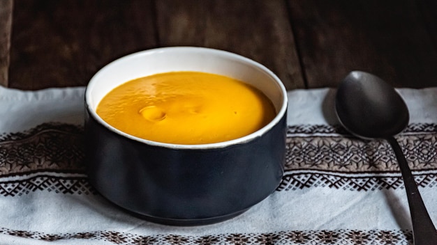 Pumpkin soup in a ceramic bowl and a napkin on a wooden table.