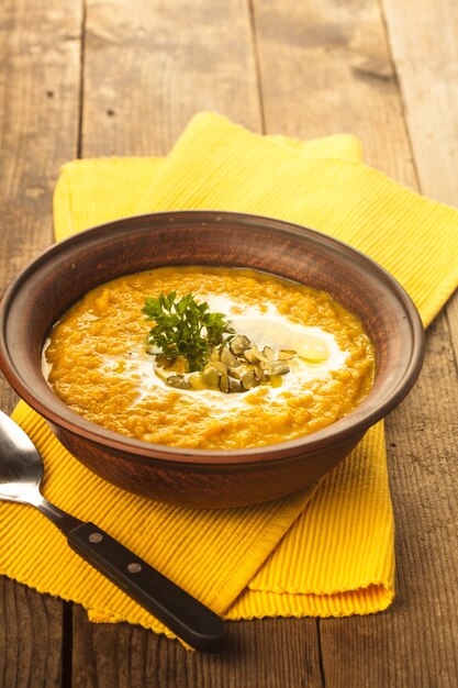 Pumpkin soup in clay bowl with spoon on the table