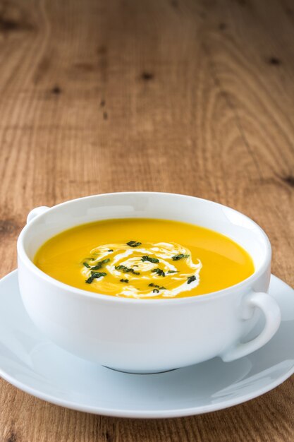 Pumpkin soup in white bowl on wooden table copy space