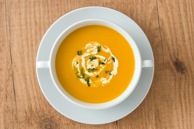 Pumpkin soup in white bowl on wooden table top view