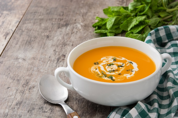 Pumpkin soup in white bowl on wooden table with copy space