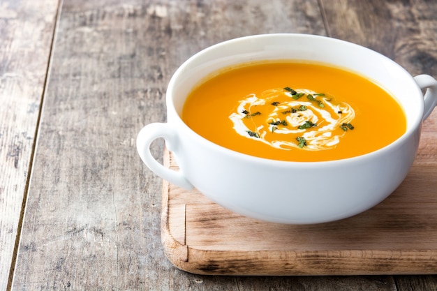 Pumpkin soup in white bowl on wooden table with copy space