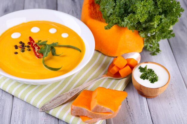 Pumpkin soup in white plate and pumpkin slice on napkin on wooden background