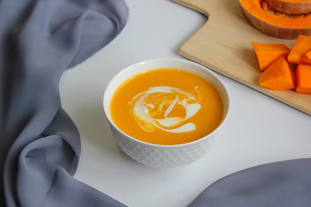 Pumpkin soup on white with gray fabric and slices of butternut squash