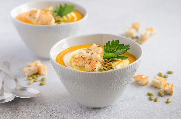 Zuppa di zucca con panna, crostini, semi di zucca e prezzemolo su cemento grigio o pietra.