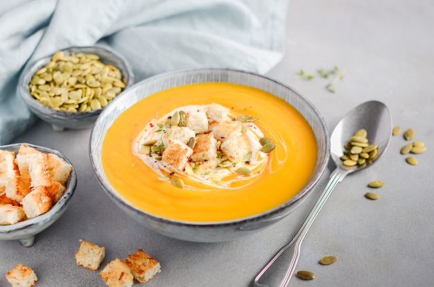 Pumpkin soup with cream, croutons, pumpkin seeds and thyme on gray concrete or stone 