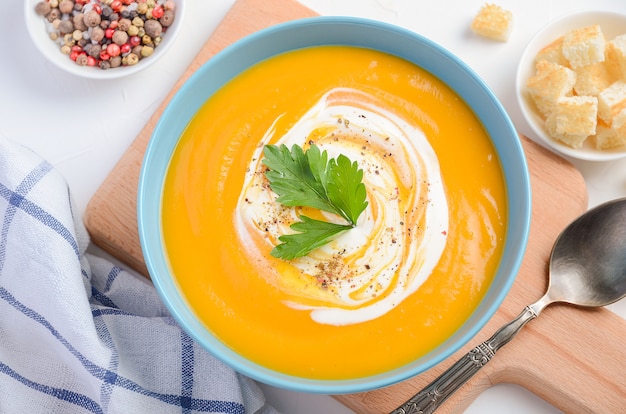 Pumpkin soup with cream and parsley on white background.