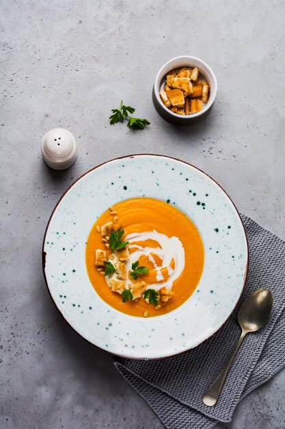 Pumpkin soup with cream, pieces of bread and cedar nuts in gray ceramic plate on gray table background. Traditional autumn food. Top view copy space.