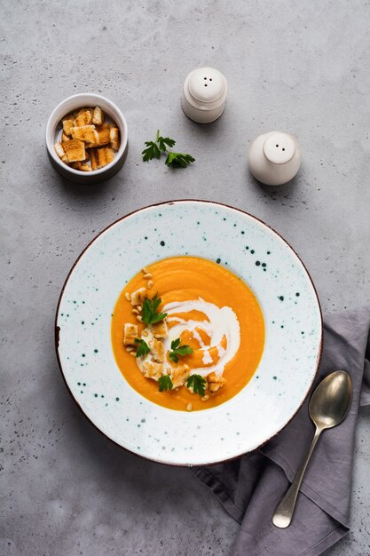 Pumpkin soup with cream, pieces of bread and cedar nuts in gray ceramic plate