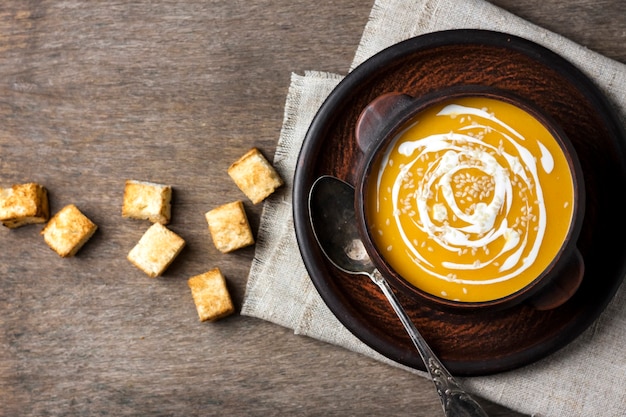 Pumpkin soup with cream and sesame seeds in brown ceramic bowl on wooden surface