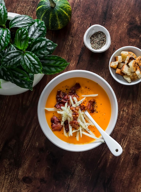 Pumpkin soup with crispy fried bacon and apple on a dark wooden background top view