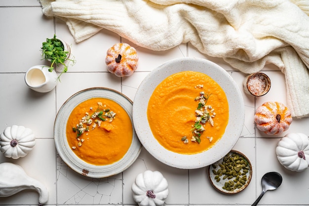 Pumpkin soup with gorgonzola cheese in white plate on white tile background top view