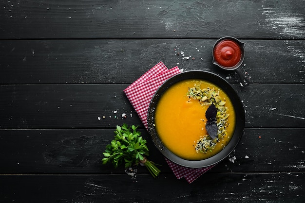 Pumpkin soup with pumpkin seeds in a black plate on a black background Top view Free space for your text