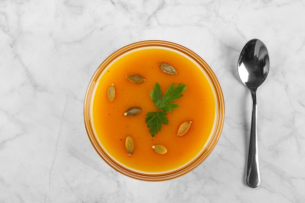 Pumpkin soup with pumpkin seeds and herbs in glass bowl on marble background