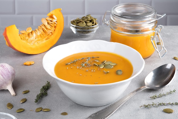 Pumpkin soup with pumpkin seeds and thyme in plate and glass jar