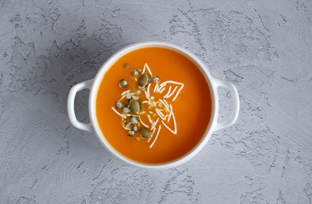 Pumpkin soup with pumpkin seeds in a white bowl on a gray background