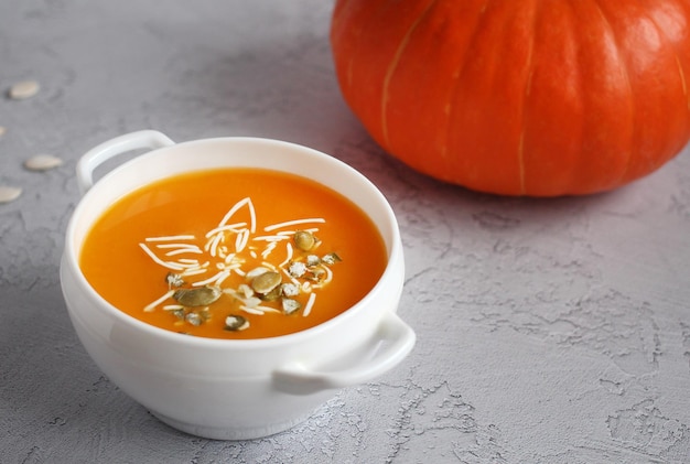 Pumpkin soup with pumpkin seeds in a white bowl on a gray background