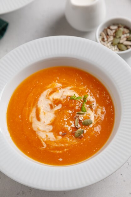 pumpkin soup with seeds and cream in a white plate on a gray table