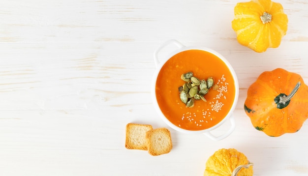 Pumpkin soup with seeds on white wooden background Top view copy space