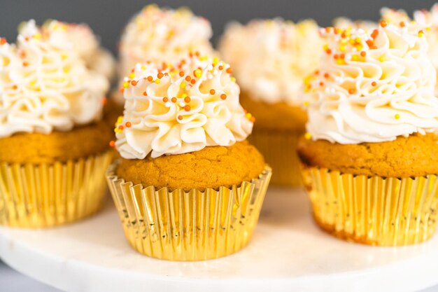 Pumpkin spice cupcake with Italian buttercream and sprinkles on a cake stand.