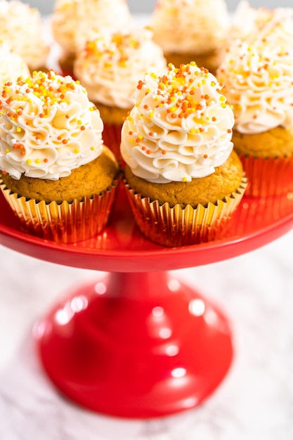 Pumpkin spice cupcake with Italian buttercream and sprinkles on a cake stand.