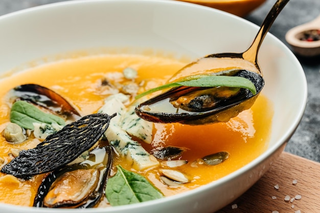 Тыквенный традиционный суп с морепродуктами, мидиями, креветками, голубым сыром, плесенью в белой миске. Предпосылка рецепта еды. Закрыть вверх
