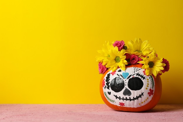 Pumpkin with catrina skull makeup and flowers on yellow background