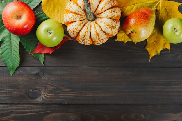 Pumpkin with colorful maple leaves, ripe apples and pear on dark wooden  background